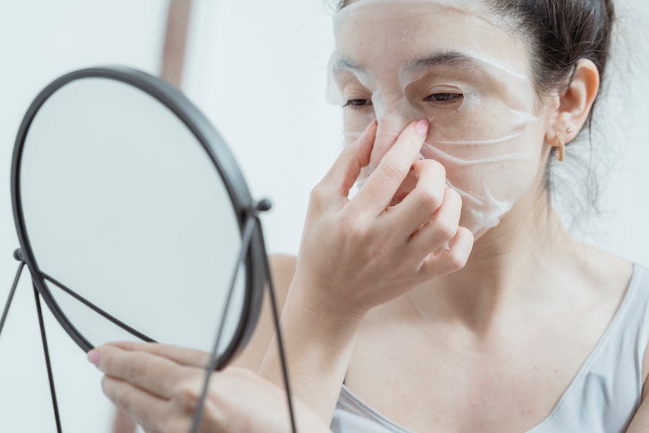 A woman in the bathroom applying a skincare facial mask while looking in a mirror
