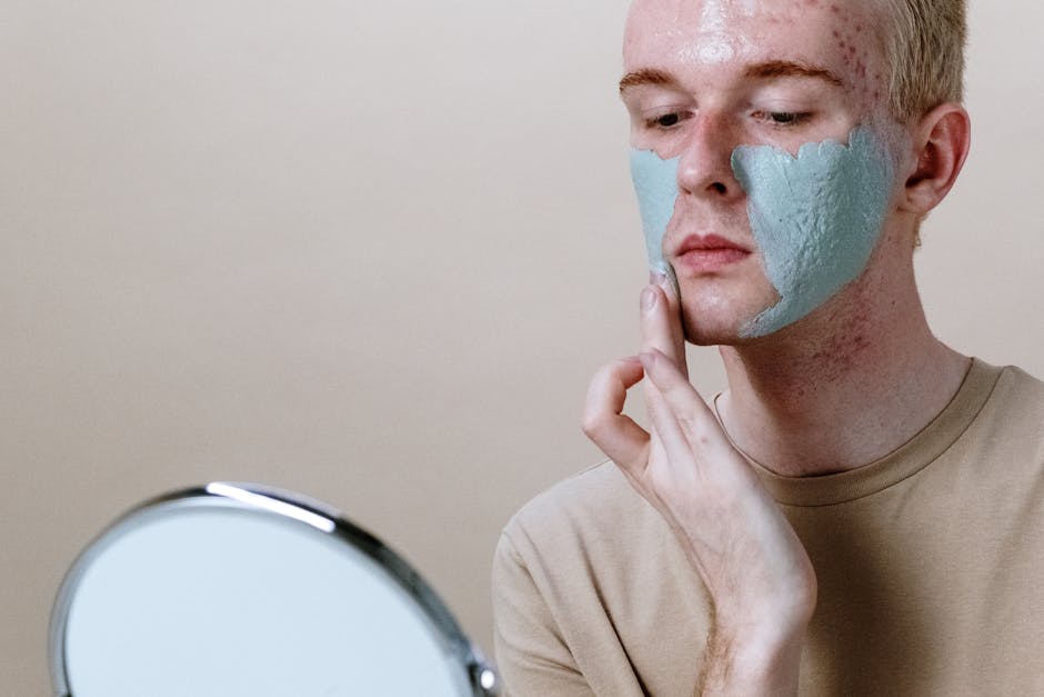 Close-up of a young man applying a clay face mask with a mirror