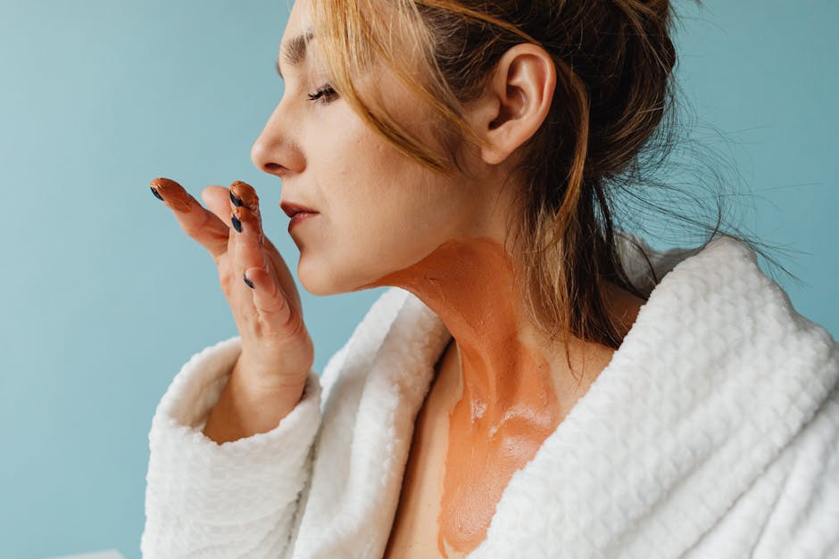 Woman in bathrobe applying face mask. Close-up wellness skincare routine